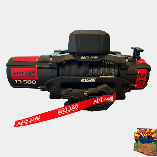 Black electric winch with red detailing, labeled MOJAB, with a capacity of 13,500 lbs. The image also includes a small inset picture depicting a celebration scene.